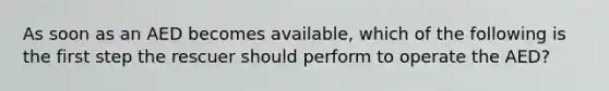 As soon as an AED becomes available, which of the following is the first step the rescuer should perform to operate the AED?