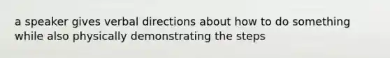 a speaker gives verbal directions about how to do something while also physically demonstrating the steps