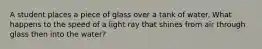 A student places a piece of glass over a tank of water. What happens to the speed of a light ray that shines from air through glass then into the water?