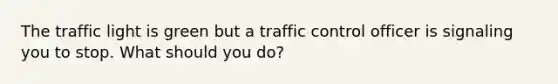 The traffic light is green but a traffic control officer is signaling you to stop. What should you do?