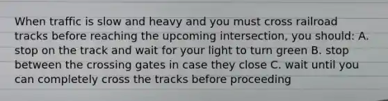 When traffic is slow and heavy and you must cross railroad tracks before reaching the upcoming intersection, you should: A. stop on the track and wait for your light to turn green B. stop between the crossing gates in case they close C. wait until you can completely cross the tracks before proceeding