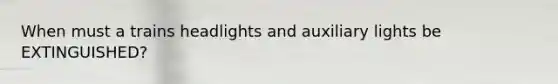 When must a trains headlights and auxiliary lights be EXTINGUISHED?