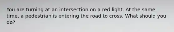 You are turning at an intersection on a red light. At the same time, a pedestrian is entering the road to cross. What should you do?