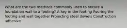 What are the two methods commonly used to secure a foundation wall to a footing? A key in the footing Pouring the footing and wall together Projecting steel dowels Construction adhesive