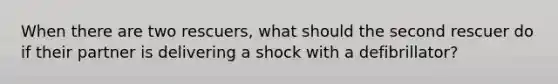 When there are two rescuers, what should the second rescuer do if their partner is delivering a shock with a defibrillator?