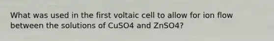 What was used in the first voltaic cell to allow for ion flow between the solutions of CuSO4 and ZnSO4?