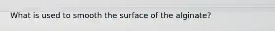 What is used to smooth the surface of the alginate?