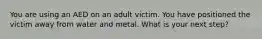 You are using an AED on an adult victim. You have positioned the victim away from water and metal. What is your next step?