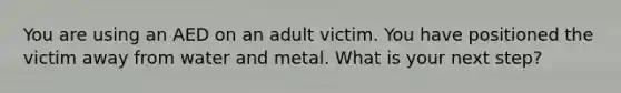 You are using an AED on an adult victim. You have positioned the victim away from water and metal. What is your next step?