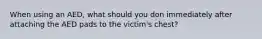 When using an AED, what should you don immediately after attaching the AED pads to the victim's chest?