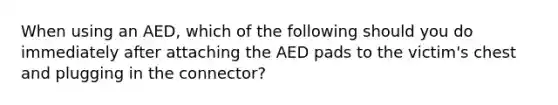 When using an AED, which of the following should you do immediately after attaching the AED pads to the victim's chest and plugging in the connector?