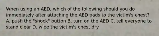 When using an AED, which of the following should you do immediately after attaching the AED pads to the victim's chest? A. push the "shock" button B. turn on the AED C. tell everyone to stand clear D. wipe the victim's chest dry