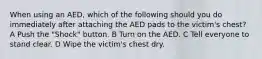 When using an AED, which of the following should you do immediately after attaching the AED pads to the victim's chest? A Push the "Shock" button. B Turn on the AED. C Tell everyone to stand clear. D Wipe the victim's chest dry.