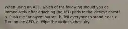 When using an AED, which of the following should you do immediately after attaching the AED pads to the victim's chest? a. Push the "Analyze" button. b. Tell everyone to stand clear. c. Turn on the AED. d. Wipe the victim's chest dry.