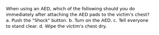 When using an AED, which of the following should you do immediately after attaching the AED pads to the victim's chest? a. Push the "Shock" button. b. Turn on the AED. c. Tell everyone to stand clear. d. Wipe the victim's chest dry.