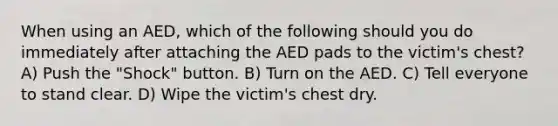 When using an AED, which of the following should you do immediately after attaching the AED pads to the victim's chest? A) Push the "Shock" button. B) Turn on the AED. C) Tell everyone to stand clear. D) Wipe the victim's chest dry.