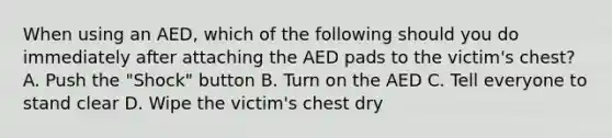 When using an AED, which of the following should you do immediately after attaching the AED pads to the victim's chest? A. Push the "Shock" button B. Turn on the AED C. Tell everyone to stand clear D. Wipe the victim's chest dry