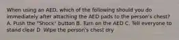 When using an AED, which of the following should you do immediately after attaching the AED pads to the person's chest? A. Push the "Shock" button B. Turn on the AED C. Tell everyone to stand clear D. Wipe the person's chest dry