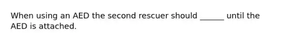 When using an AED the second rescuer should ______ until the AED is attached.