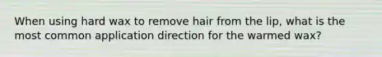 When using hard wax to remove hair from the lip, what is the most common application direction for the warmed wax?