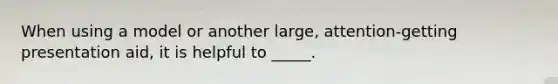 When using a model or another large, attention-getting presentation aid, it is helpful to _____.