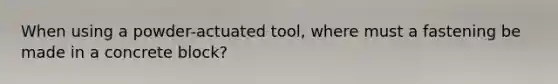 When using a powder-actuated tool, where must a fastening be made in a concrete block?