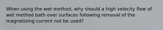 When using the wet method, why should a high velocity flow of wet method bath over surfaces following removal of the magnetizing current not be used?