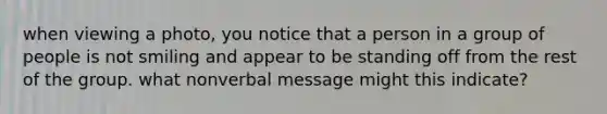 when viewing a photo, you notice that a person in a group of people is not smiling and appear to be standing off from the rest of the group. what nonverbal message might this indicate?