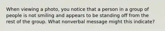 When viewing a photo, you notice that a person in a group of people is not smiling and appears to be standing off from the rest of the group. What nonverbal message might this indicate?