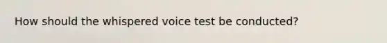 How should the whispered voice test be conducted?