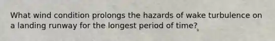 What wind condition prolongs the hazards of wake turbulence on a landing runway for the longest period of time?