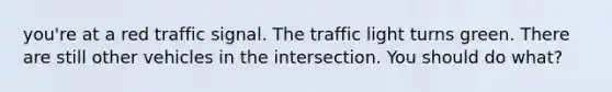 you're at a red traffic signal. The traffic light turns green. There are still other vehicles in the intersection. You should do what?