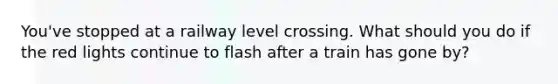 You've stopped at a railway level crossing. What should you do if the red lights continue to flash after a train has gone by?