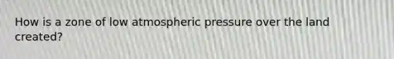 How is a zone of low atmospheric pressure over the land created?